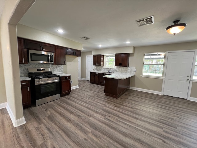 kitchen with hardwood / wood-style floors, sink, decorative backsplash, light stone countertops, and stainless steel appliances