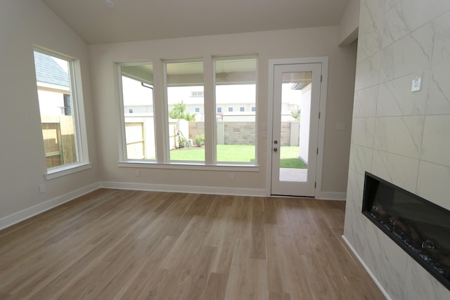 interior space with a tile fireplace, light hardwood / wood-style floors, vaulted ceiling, and a healthy amount of sunlight