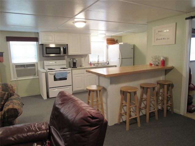 kitchen featuring white cabinets, plenty of natural light, a kitchen bar, and white appliances