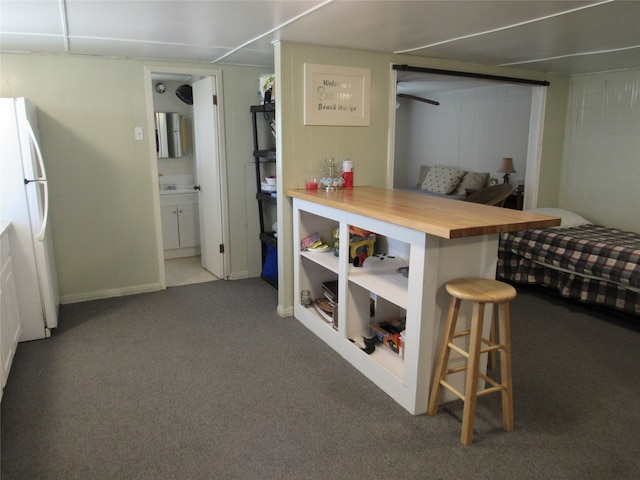 interior space featuring white cabinetry, carpet flooring, a breakfast bar, white fridge, and wooden counters