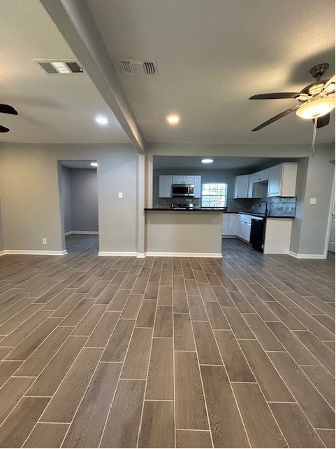 unfurnished living room with sink, ceiling fan, hardwood / wood-style floors, and beamed ceiling