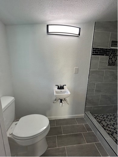 bathroom with tile patterned flooring, toilet, a tile shower, and a textured ceiling