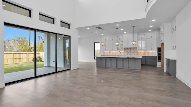 kitchen featuring gray cabinetry, hanging light fixtures, tasteful backsplash, a kitchen island with sink, and appliances with stainless steel finishes