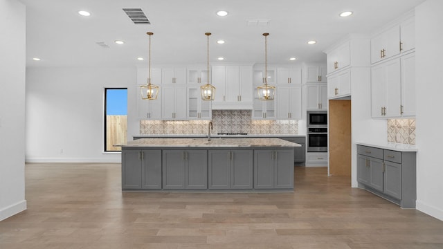 kitchen featuring gray cabinetry, hanging light fixtures, light hardwood / wood-style floors, a kitchen island with sink, and appliances with stainless steel finishes