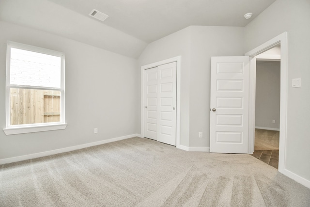 unfurnished bedroom featuring vaulted ceiling, light carpet, and a closet