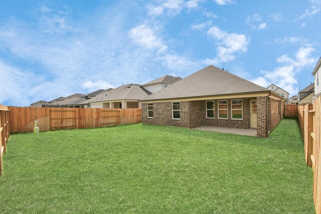 back of house with a fenced backyard, a yard, brick siding, roof with shingles, and a patio area