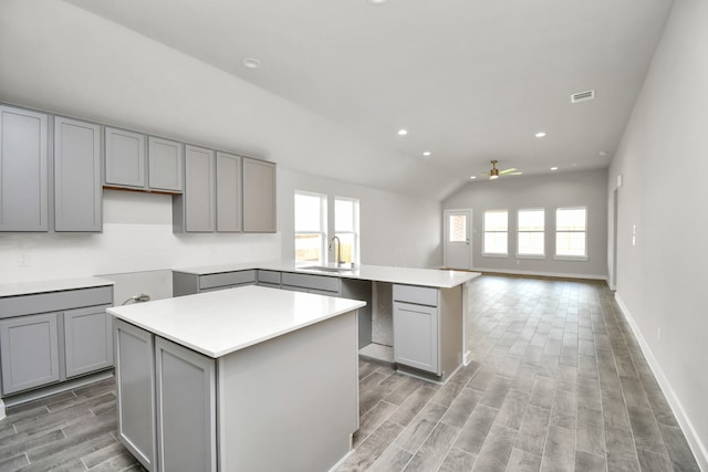 kitchen with gray cabinets, lofted ceiling, a center island, ceiling fan, and sink