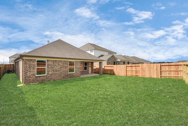 back of property featuring a yard, a shingled roof, brick siding, and a fenced backyard
