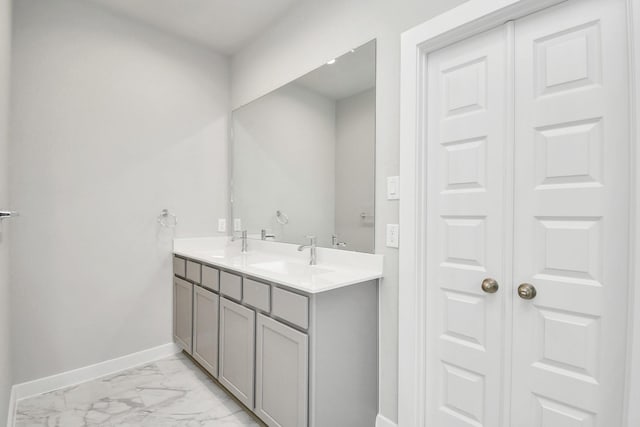 bathroom with baseboards, marble finish floor, double vanity, and a sink