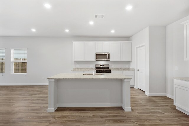 kitchen with light stone counters, light wood-type flooring, stainless steel appliances, and a kitchen island with sink