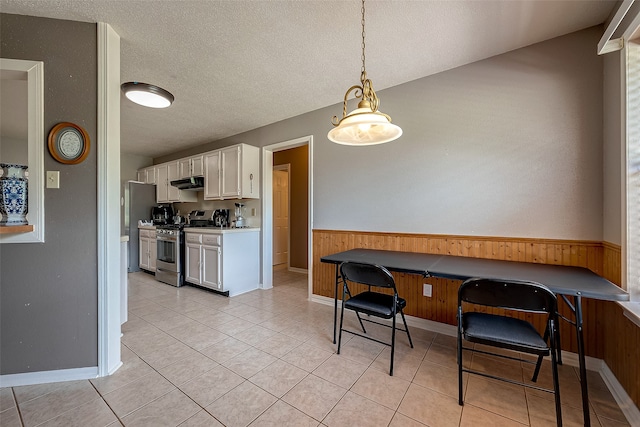 kitchen with light tile patterned flooring, stainless steel gas stove, ventilation hood, pendant lighting, and white cabinets