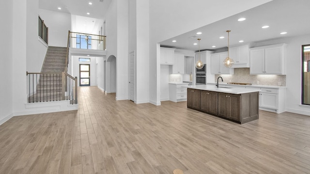 kitchen with pendant lighting, an island with sink, light hardwood / wood-style flooring, and white cabinets