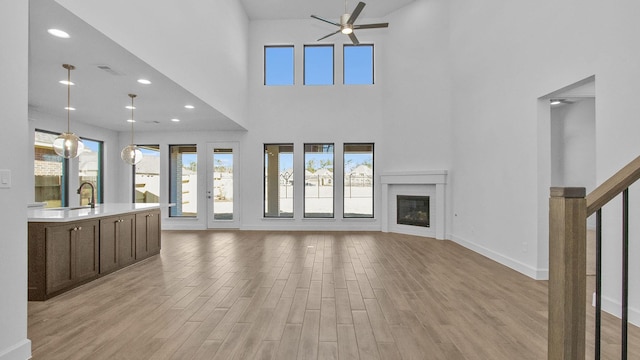 unfurnished living room featuring ceiling fan, light hardwood / wood-style floors, sink, and a high ceiling