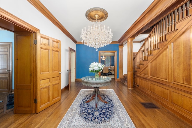 foyer entrance featuring ornate columns, hardwood / wood-style flooring, crown molding, and an inviting chandelier