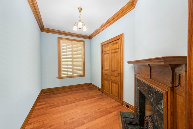 entrance foyer with a fireplace, ornamental molding, an inviting chandelier, and light wood-type flooring