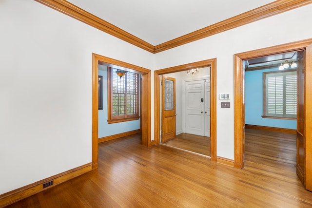 empty room with a wealth of natural light, crown molding, and wood-type flooring