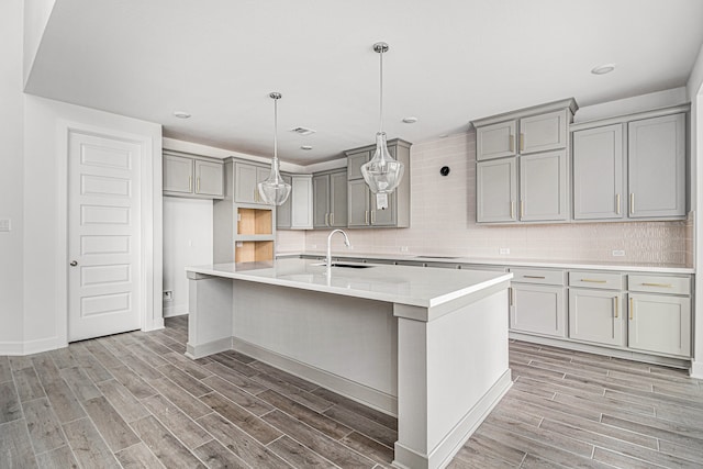 kitchen featuring hardwood / wood-style floors, sink, decorative backsplash, and a center island with sink