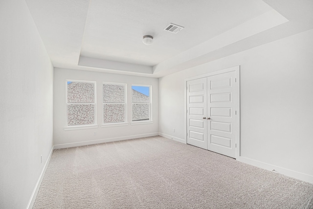 unfurnished bedroom featuring carpet flooring, a closet, and a tray ceiling