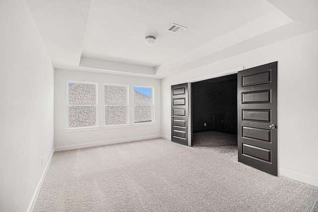 unfurnished bedroom with carpet floors and a tray ceiling