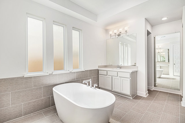 bathroom with tile patterned flooring, tile walls, vanity, a bathtub, and plenty of natural light