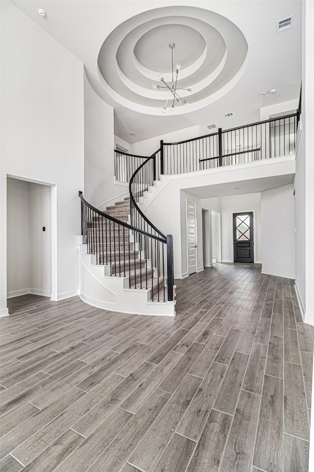 stairs featuring a tray ceiling, a notable chandelier, hardwood / wood-style flooring, and a towering ceiling