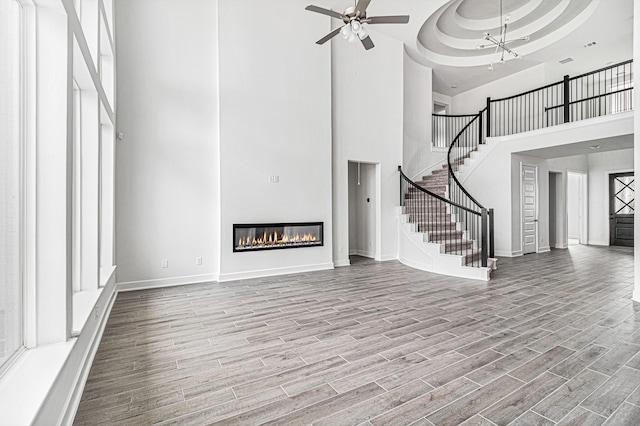 unfurnished living room featuring a raised ceiling, ceiling fan with notable chandelier, hardwood / wood-style floors, and a high ceiling