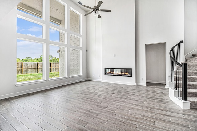 unfurnished living room featuring a towering ceiling, light wood-type flooring, and ceiling fan