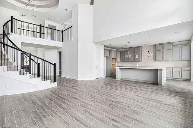 unfurnished living room with sink, light hardwood / wood-style flooring, and a towering ceiling