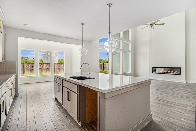 kitchen featuring light hardwood / wood-style floors, decorative backsplash, sink, a kitchen island with sink, and hanging light fixtures