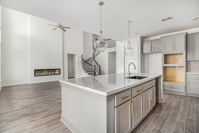 kitchen featuring sink, wood-type flooring, a kitchen island with sink, ceiling fan, and gray cabinets