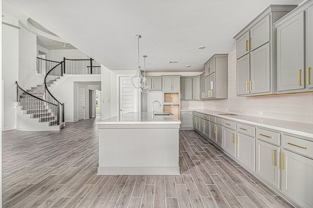 kitchen featuring backsplash, sink, wood-type flooring, a kitchen island with sink, and gray cabinets