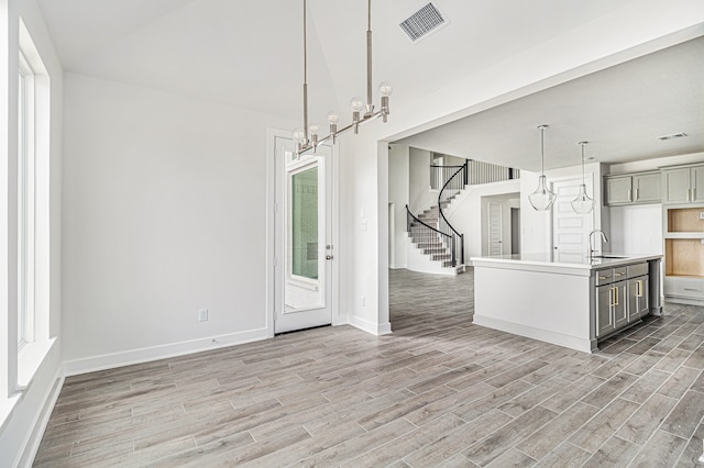 unfurnished living room featuring sink, light wood-type flooring, and an inviting chandelier