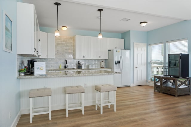 kitchen featuring decorative backsplash, white refrigerator with ice dispenser, white cabinets, and light hardwood / wood-style floors