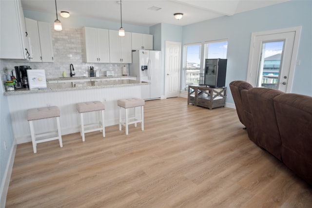 kitchen featuring a breakfast bar area, backsplash, white fridge with ice dispenser, light wood-type flooring, and white cabinets