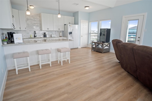 833 S Oneal Rd, Crystal Beach, TX 77650 - kitchen with white refrigerator with ice dispenser, a breakfast bar area, a peninsula, light wood-style floors, and backsplash