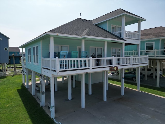 rear view of house with concrete driveway, a lawn, a balcony, roof with shingles, and a carport