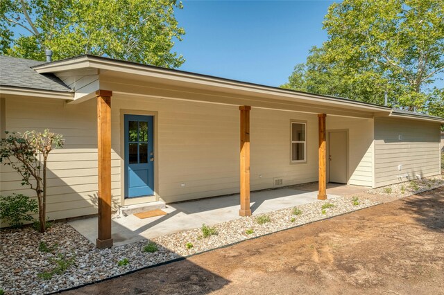 entrance to property with roof with shingles and a patio area