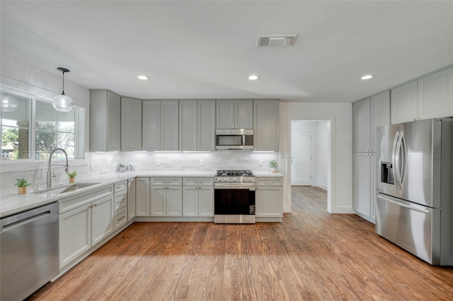 kitchen featuring stainless steel appliances, visible vents, decorative backsplash, light wood-style floors, and a sink