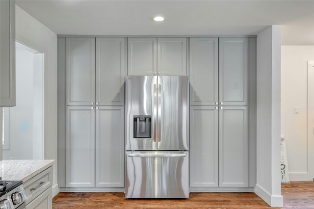 kitchen with stainless steel refrigerator with ice dispenser, gray cabinets, stove, light wood-style floors, and light stone countertops