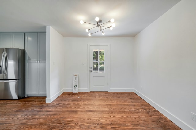 unfurnished dining area featuring a notable chandelier, baseboards, and wood finished floors