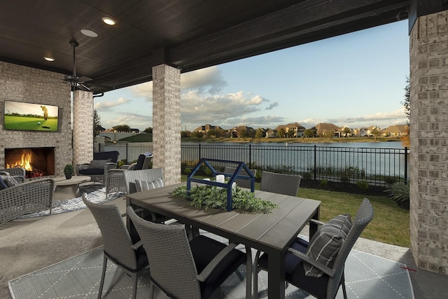 view of patio featuring outdoor dining area, an outdoor stone fireplace, a water view, and a fenced backyard