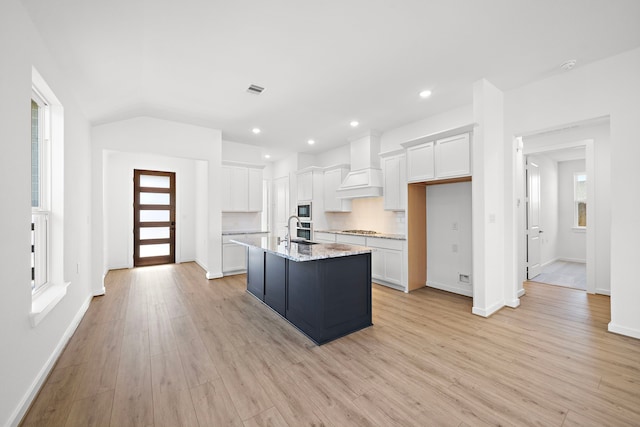 kitchen featuring a wealth of natural light, custom range hood, white cabinetry, and a sink