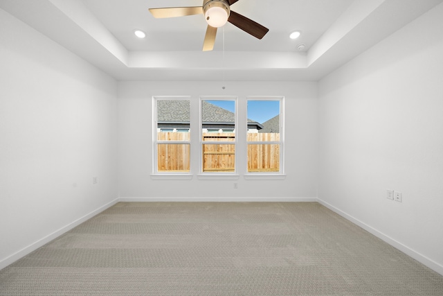 spare room featuring a raised ceiling, carpet flooring, ceiling fan, and baseboards