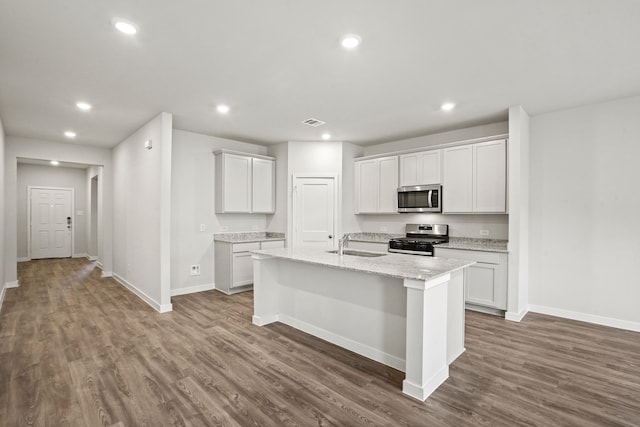 kitchen featuring an island with sink, white cabinets, light stone countertops, and stainless steel appliances