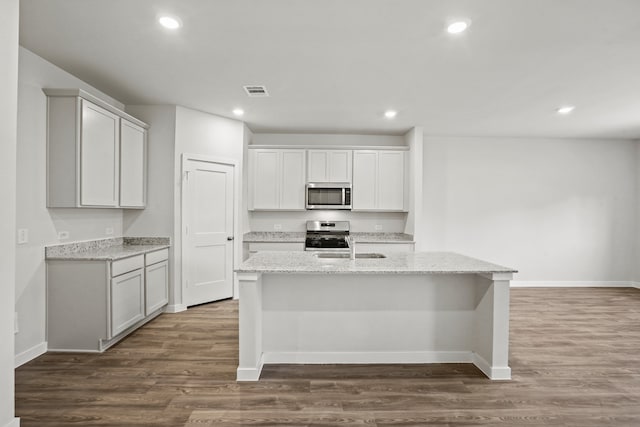 kitchen with light stone countertops, a center island with sink, appliances with stainless steel finishes, and dark wood-type flooring