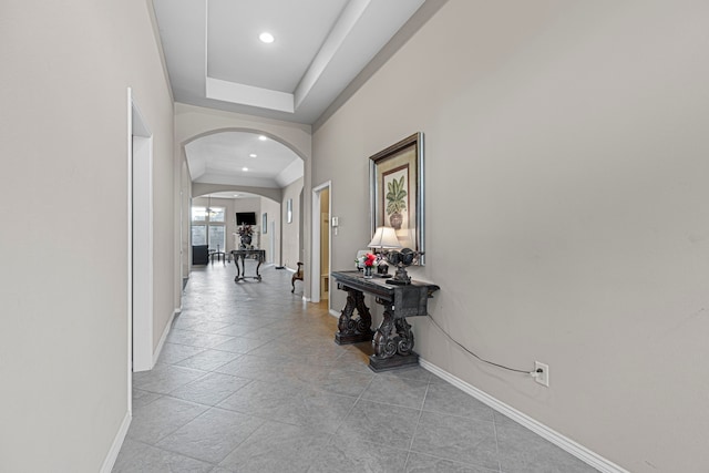 hallway with a tray ceiling and light tile patterned flooring