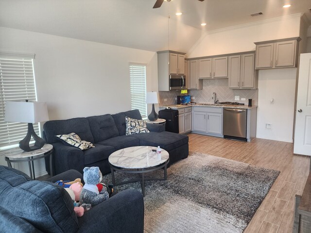 living room featuring light wood-type flooring, ceiling fan, crown molding, sink, and lofted ceiling