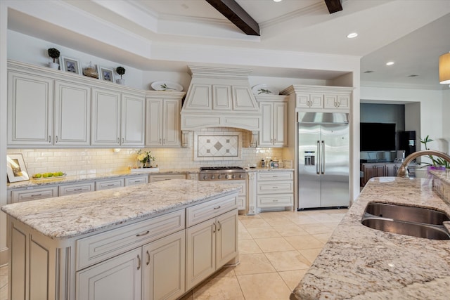 kitchen featuring premium range hood, beam ceiling, appliances with stainless steel finishes, light stone counters, and sink