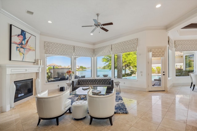 tiled living room with ceiling fan, a tiled fireplace, crown molding, and a water view