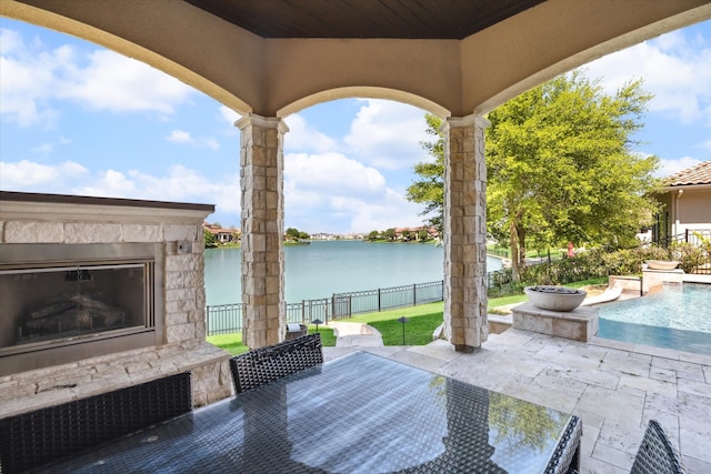 view of patio / terrace with a fenced in pool, an outdoor stone fireplace, and a water view